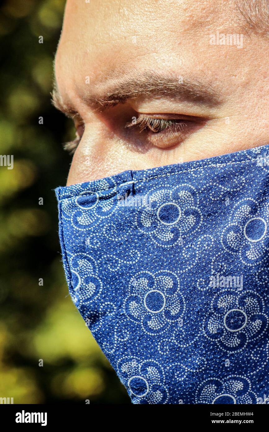 Jeune homme blanc barbu avec un masque de visage en tissu bleu pendant la pandémie de coronavirus. Coronavirus, éclosion de COVID-19. Prévenir le concept de grippe. Arrière-plan flou. Photo verticale. Banque D'Images