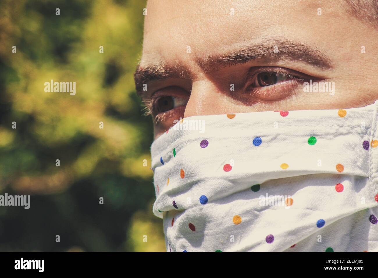 Jeune homme blanc avec un masque fait main en tissu pendant la pandémie de coronavirus. Coronavirus, éclosion de COVID-19. Concept de protection antivirus. Arrière-plan flou. Détail visage et yeux. Banque D'Images