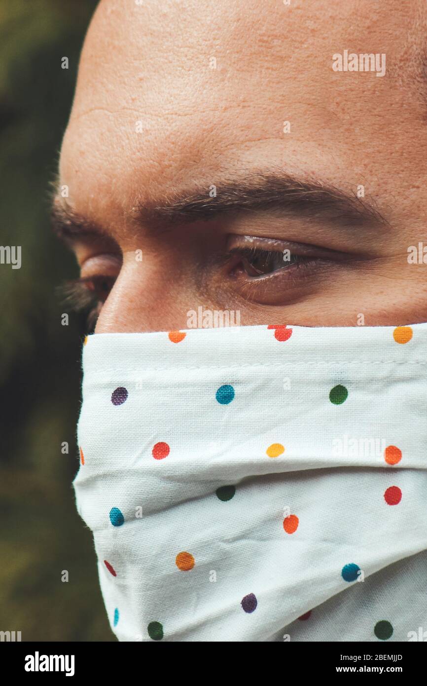 Jeune homme blanc avec un masque fait main en tissu pendant la pandémie de coronavirus. Coronavirus, éclosion de COVID-19. Concept de protection antivirus. Arrière-plan flou. Détail visage et yeux. Banque D'Images