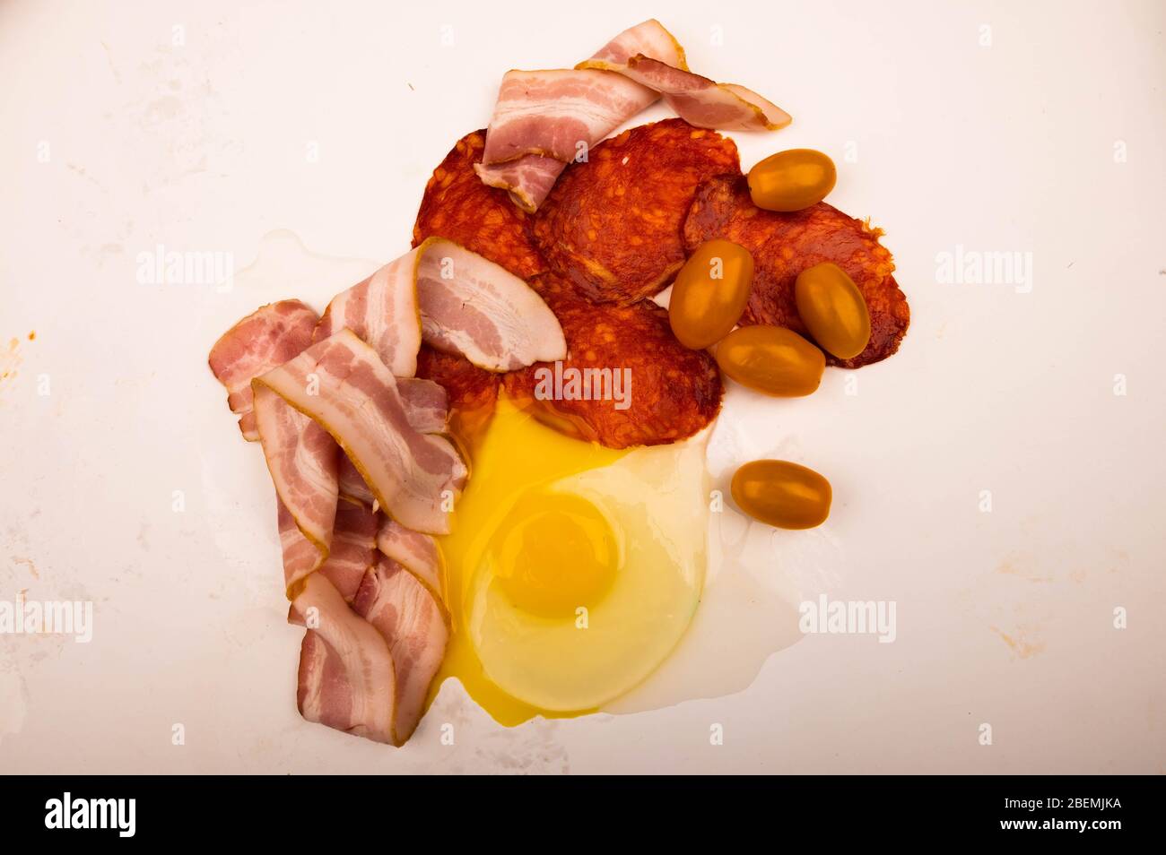 Oeuf de poulet cassé, tranches de bacon, saucisses et tomates sur fond blanc. Gros plan Banque D'Images