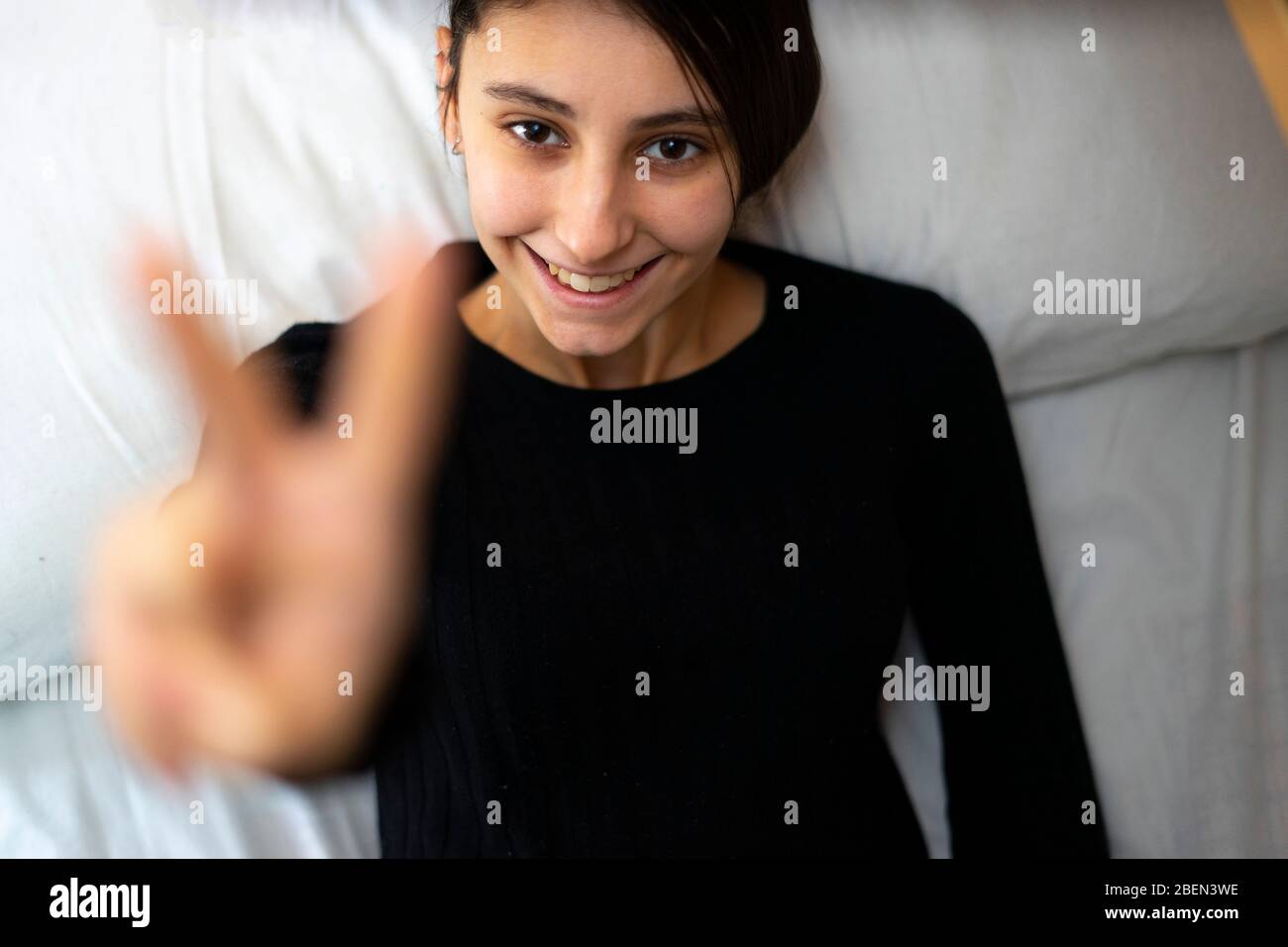Femme au lit montrant la main avec deux doigts vers le haut en paix ou symbole de victoire. Banque D'Images