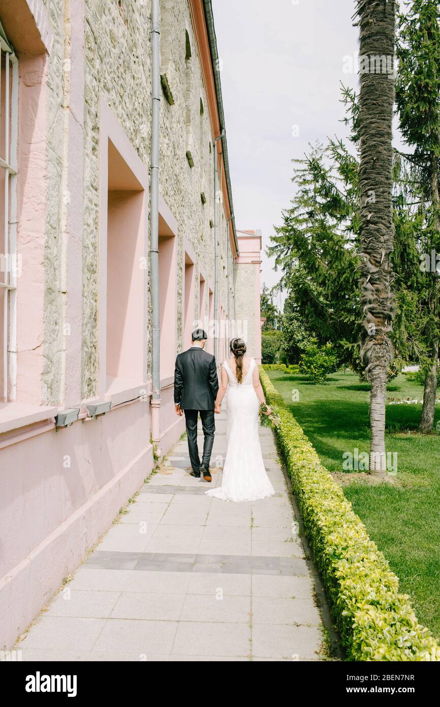 La mariée pose le marié. Ils marchent avec un dos-à-dos à côté d'un bâtiment historique. La mariée a une fleur dans sa main. La mariée et le marié sont heureux. Banque D'Images