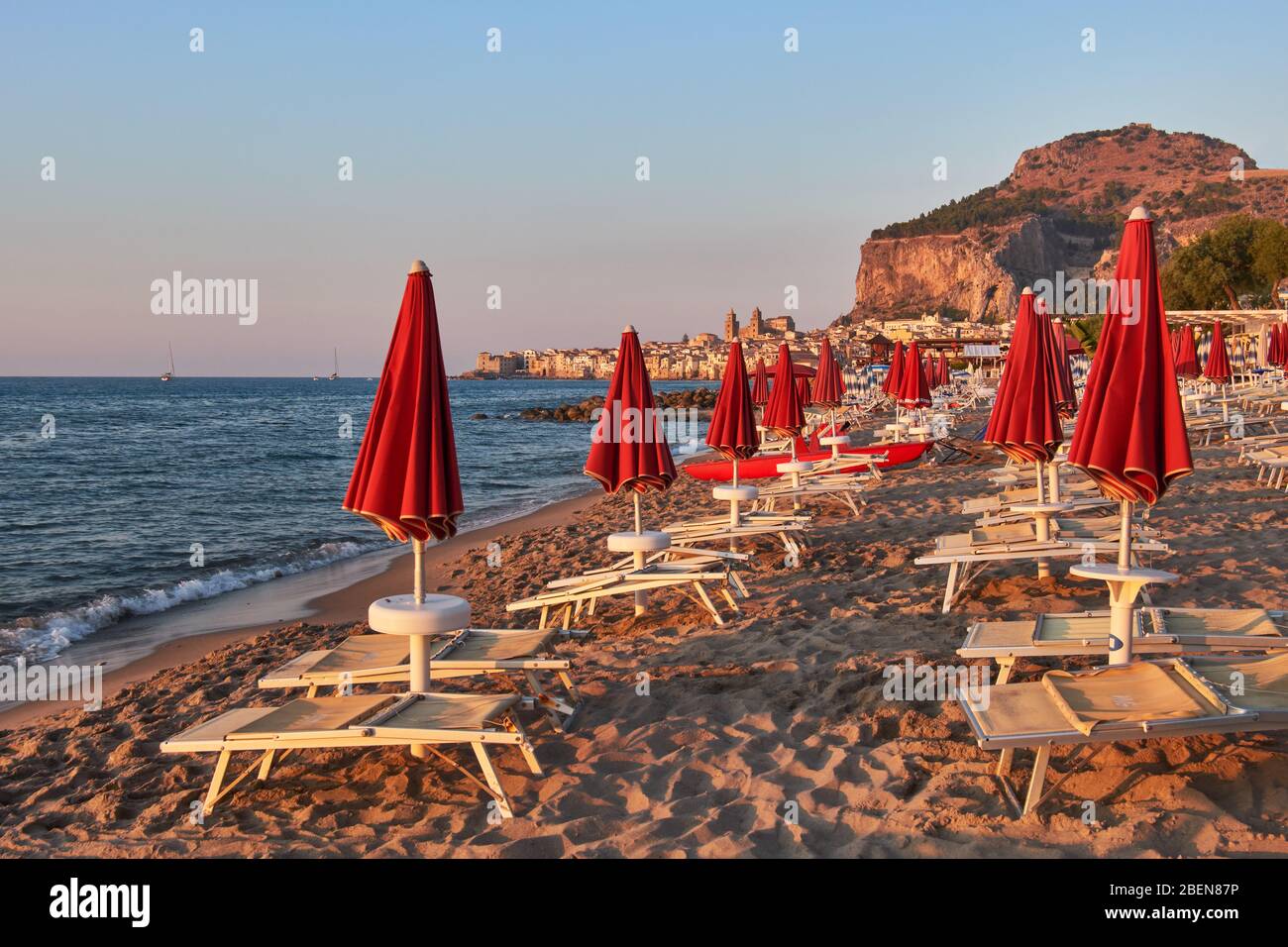 Dans l'atmosphère de crépuscule, des parasols fermés devant la ville de Cefalù avec son célèbre rocher Banque D'Images