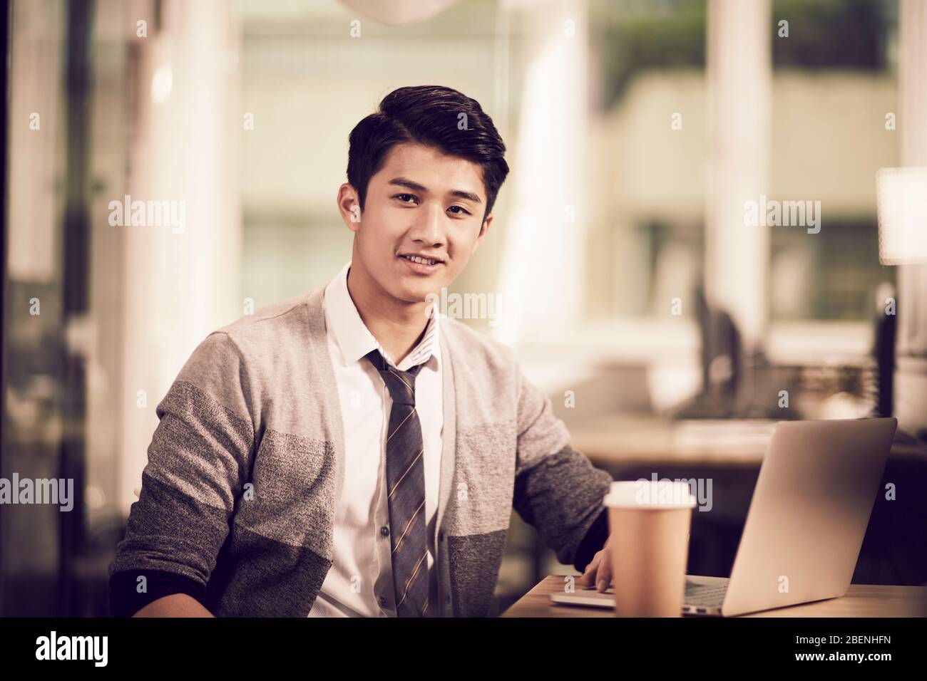portrait d'un jeune entrepreneur asiatique réussi assis à un bureau en regardant un appareil photo souriant Banque D'Images