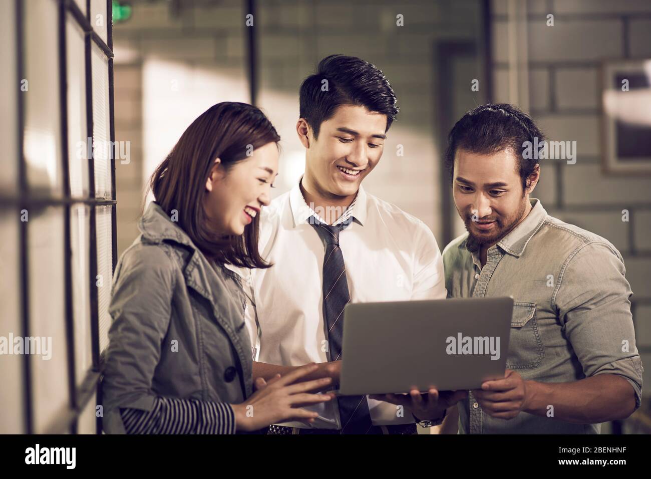 une équipe de trois jeunes entrepreneurs asiatiques en affaires regardant ensemble ordinateur portable au bureau Banque D'Images