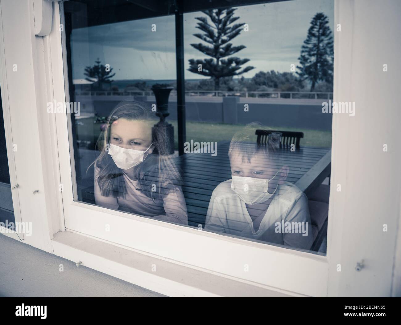 Verrouillages COVID-19. Enfants tristes avec masque de visage regardant par la fenêtre pendant la quarantaine à la maison. Les enfants se sentent tristes car l'école est fermée. Coronaviru Banque D'Images