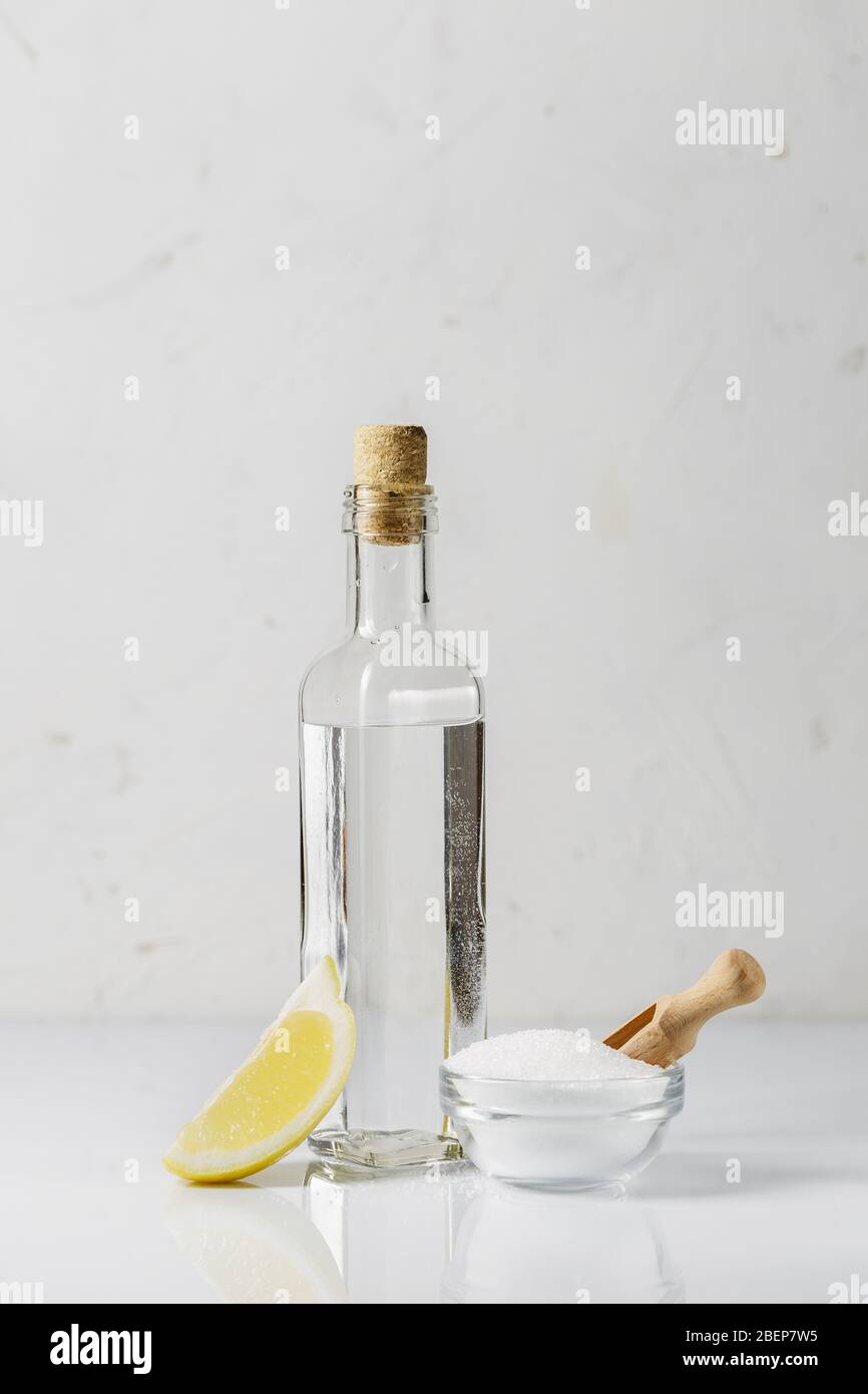 Acide citrique dans un petit bol en verre, vinaigre blanc dans une bouteille et une tranche de citron sur fond lumineux, ingrédients de produit de nettoyage Banque D'Images