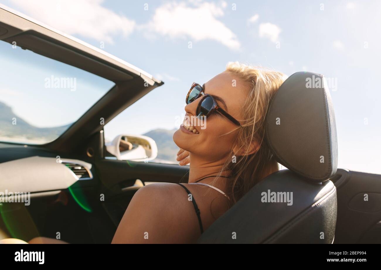 Jolie jeune femme assise sur le siège passager avant d'une voiture et souriante. Femme voyageant en voiture convertible en voyage sur route. Banque D'Images