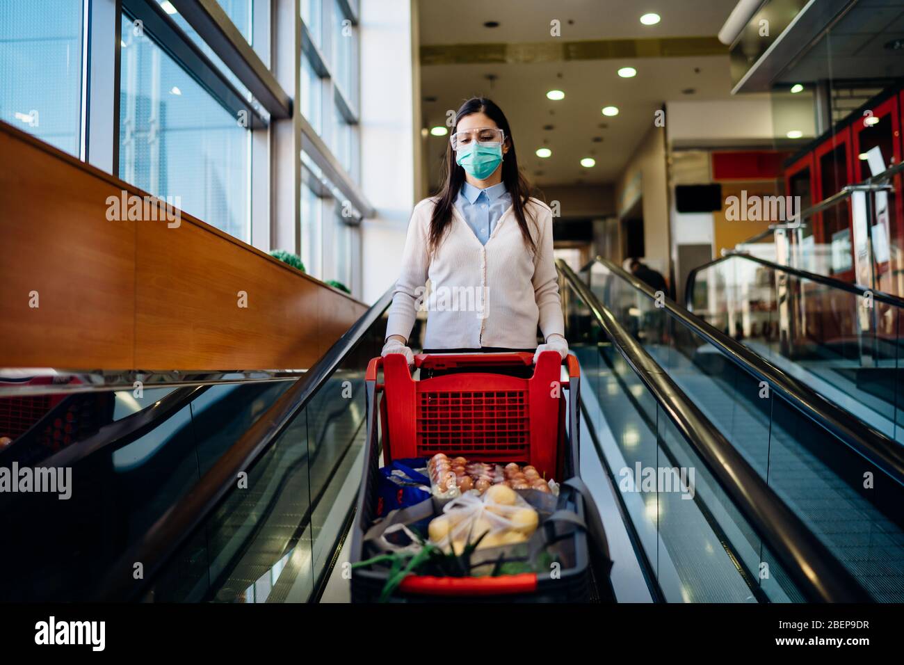 Femme portant des magasins d'épicerie masque dans un supermarché, chariot de poussée.Achat et hoarding de panique alimentaire.Covid-19 stock de quarantaine avec panier.sus Banque D'Images