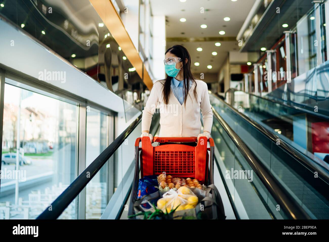 Femme portant des magasins d'épicerie masque dans un supermarché, chariot de poussée.Achat et hoarding de panique alimentaire.Covid-19 stock de quarantaine avec panier.sus Banque D'Images