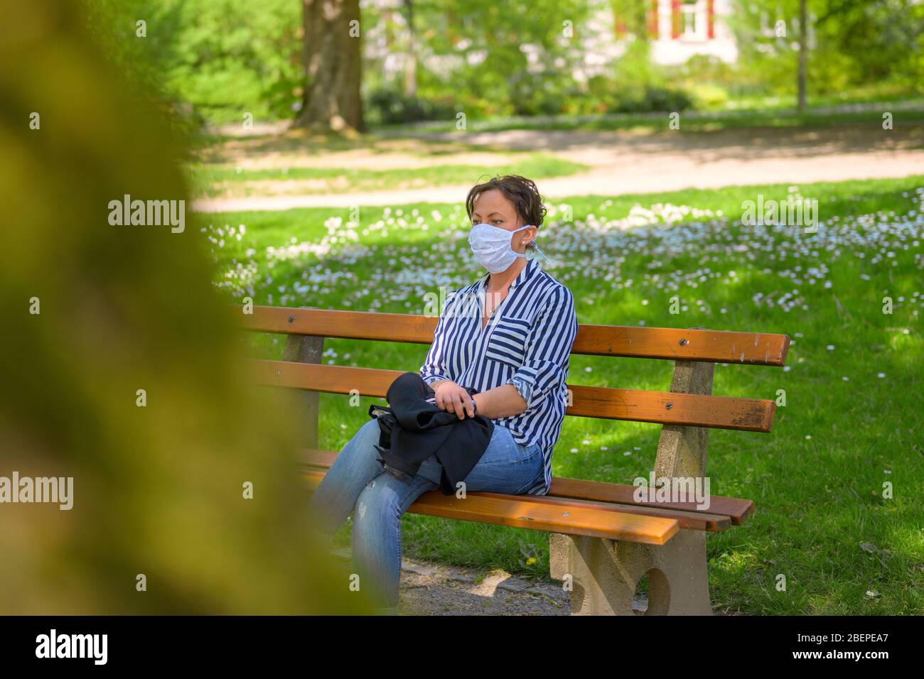 Femme se reposant sur un banc de parc portant un masque chirurgical contre une infection ou une propagation possible du coronavirus ou du Covid-19 pendant la pandémie Banque D'Images