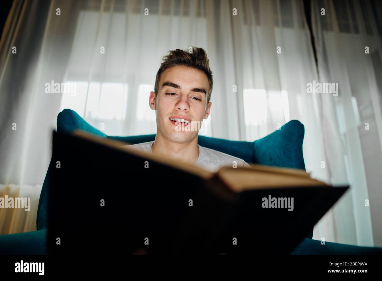 Homme appréciant la lecture d'un livre intéressant, maison seule en quarantaine.soins de santé mentale auto-soins, détente à la maison activité.étudier,apprendre,éducation.réduire Banque D'Images