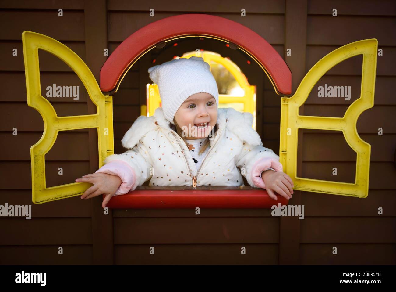Portrait drôle de fille de bébé regardant par la fenêtre de maison de jouet. Banque D'Images