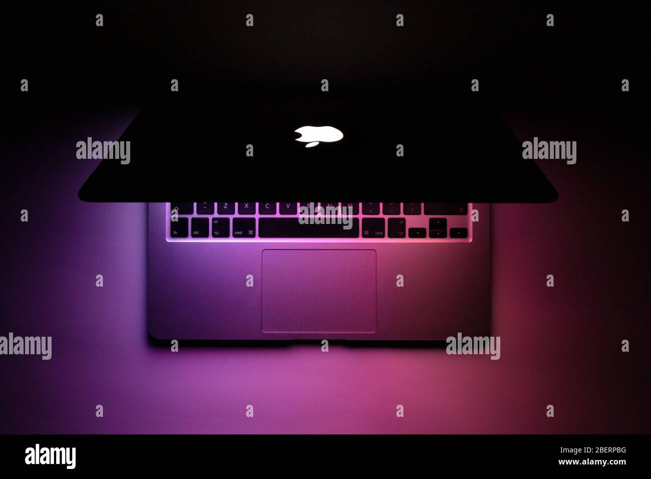 un macbook à moitié fermé avec une lueur violette dans l'obscurité Banque D'Images