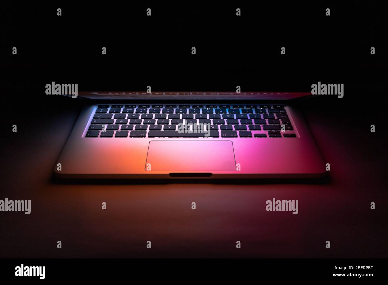 un ordinateur portable a été fermé à moitié dans le noir avec une lumière colorée Banque D'Images