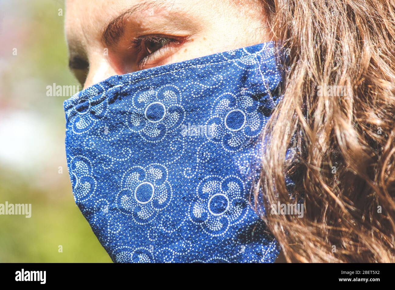 Jeune femme caucasienne à l'extérieur avec un masque de visage en tissu bleu pendant la pandémie de coronavirus. Coronavirus, éclosion de COVID-19. Concept de protection antivirus. Arrière-plan flou. Banque D'Images