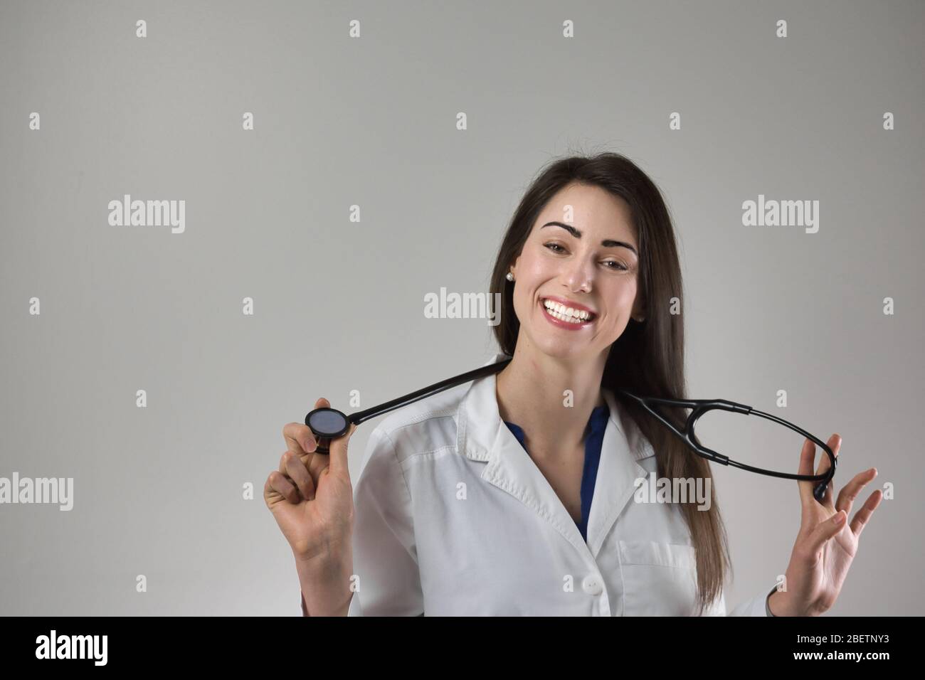 Professionnel de la santé féminin tenant stéthoscope autour du cou isolé sur fond gris. Jolie jeune femme avec un beau sourire. Banque D'Images