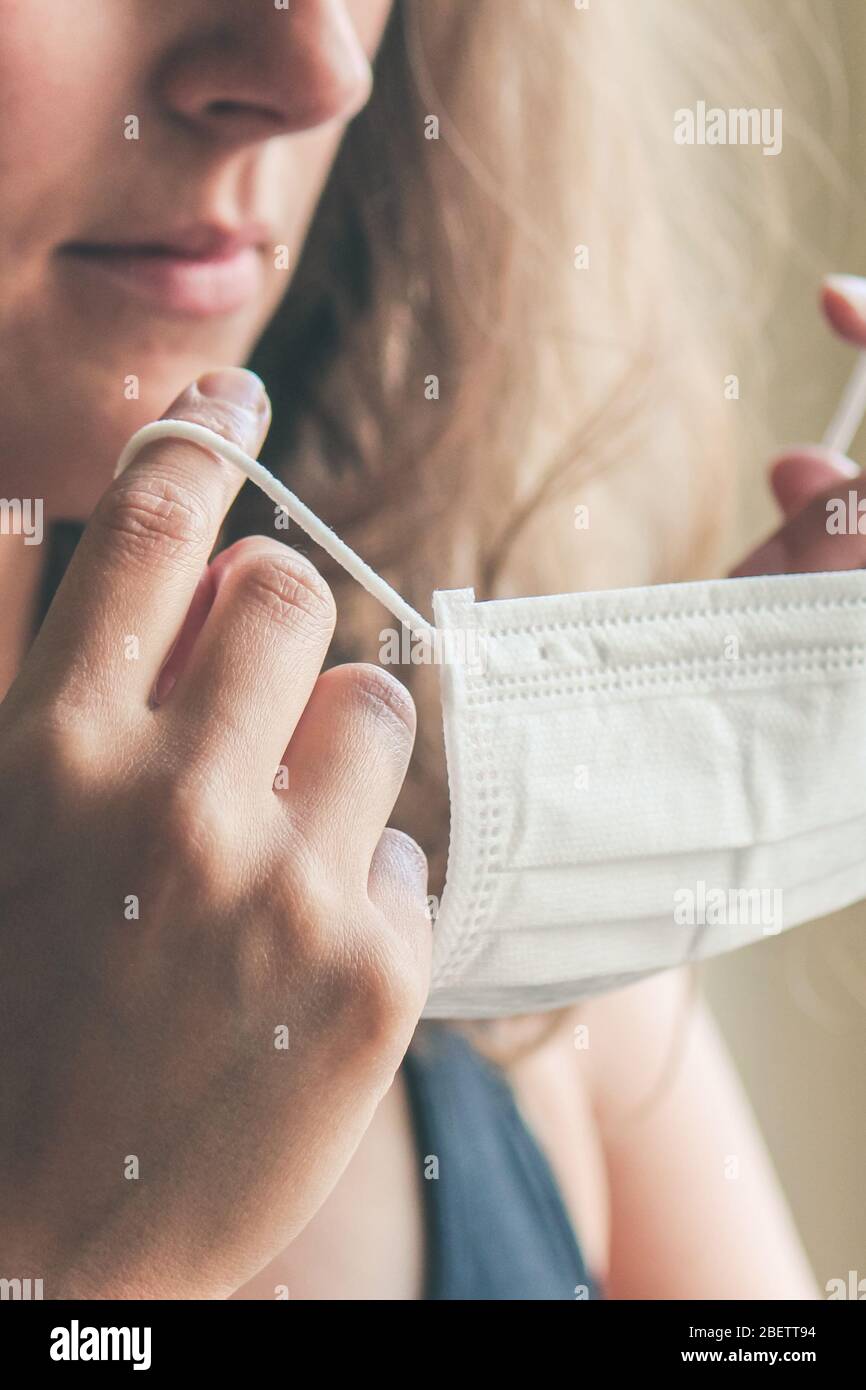 Photo détaillée d'une femme blanche non reconnaissable mettant sur un masque médical blanc pour prévenir l'infection. Fond flou, foyer sur le masque. Coronavirus, COVID-19 quarantaine. Concept de verrouillage. Banque D'Images