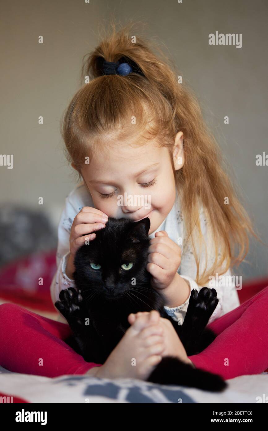 Portrait d'une petite fille d'enfant mignonne qui hople un chat noir avec  tendresse et amour et sourires avec bonheur Photo Stock - Alamy