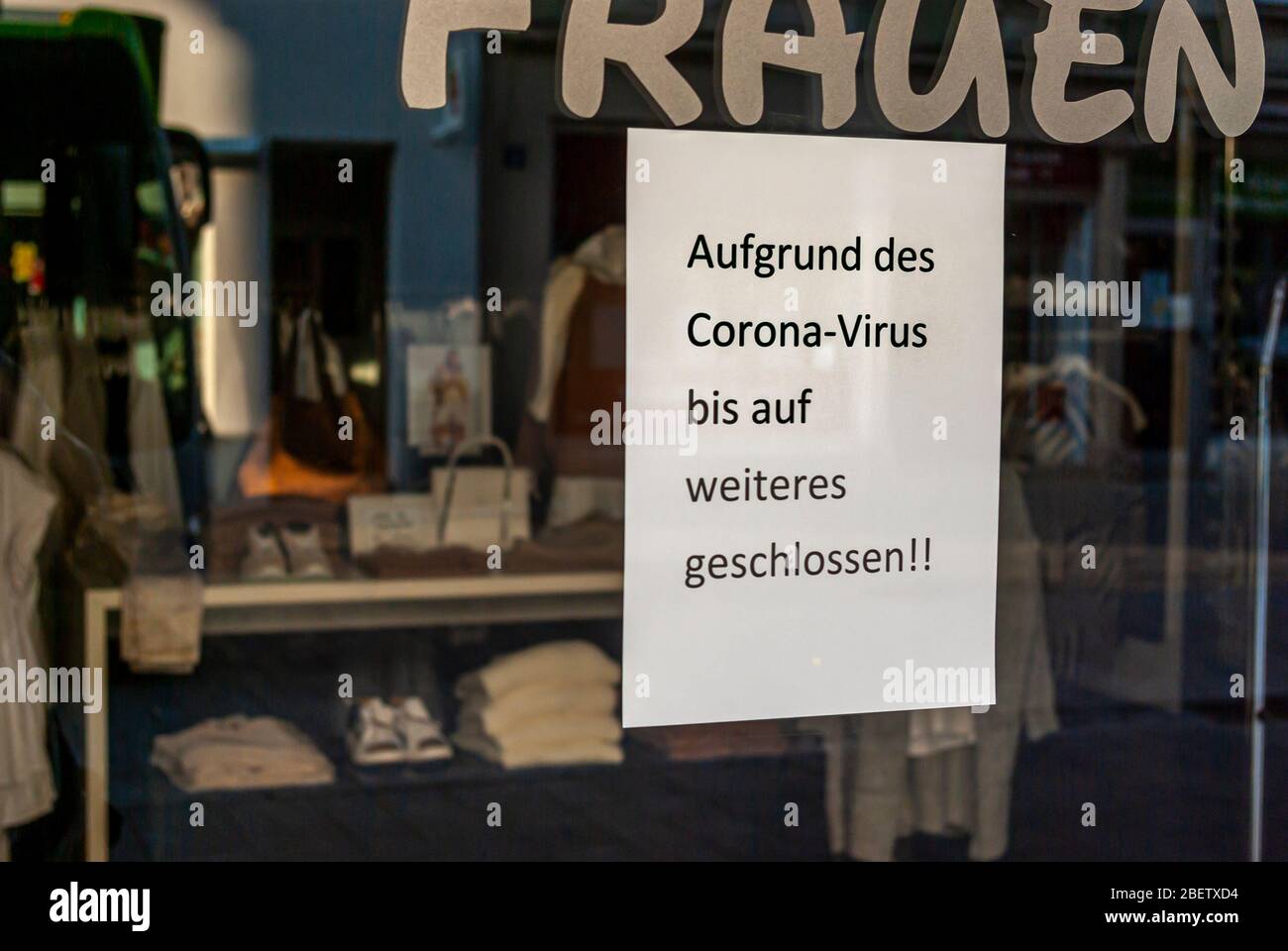 Fenêtre de boutique d'une boutique avec un signe 'fermé à cause du virus Corona', en allemand, avec des écrans et le reflet de l'environnement en flou à la Banque D'Images