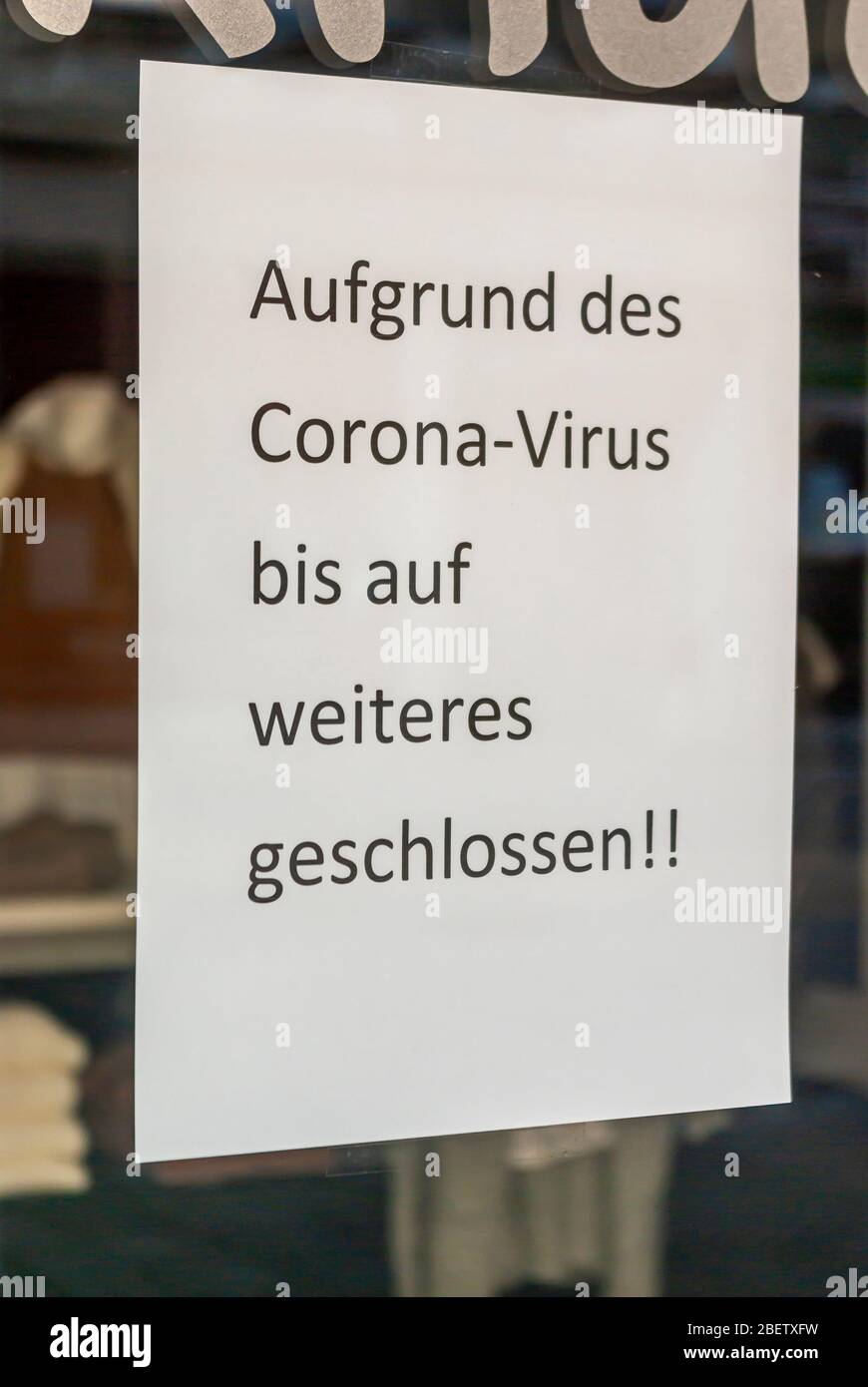 Fenêtre de boutique d'une boutique avec un signe 'fermé à cause du virus Corona', en allemand, avec des écrans et le reflet de l'environnement en flou à la Banque D'Images