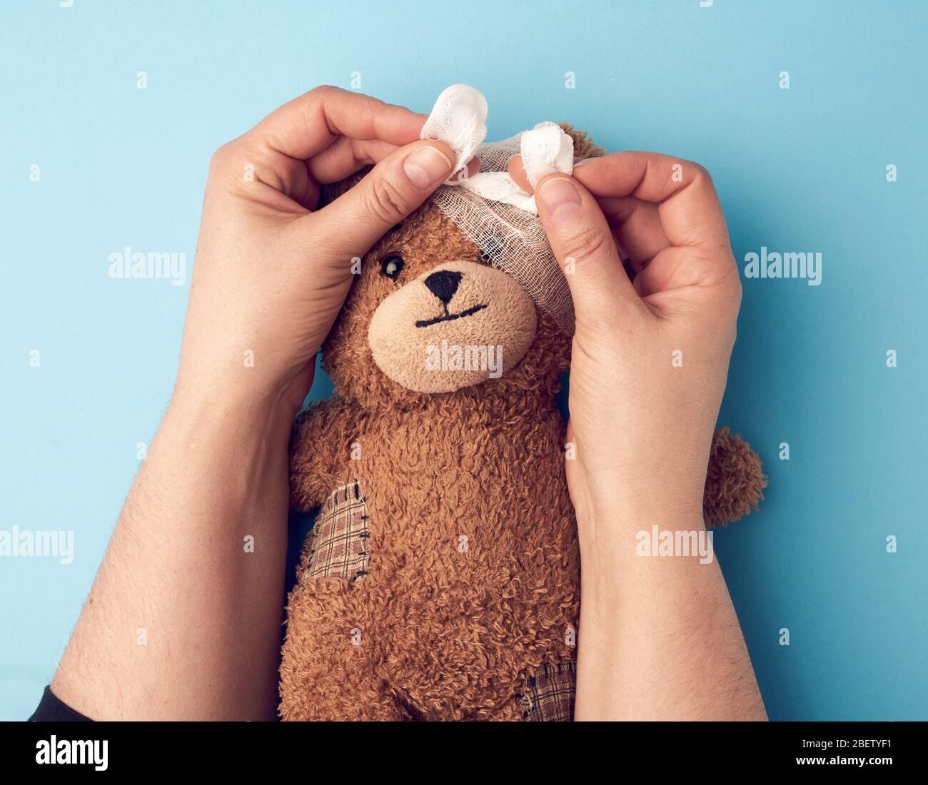 deux mains rembobinent la tête avec une gaze blanche bandage médical à un ours brun en peluche, assistance médicale Banque D'Images