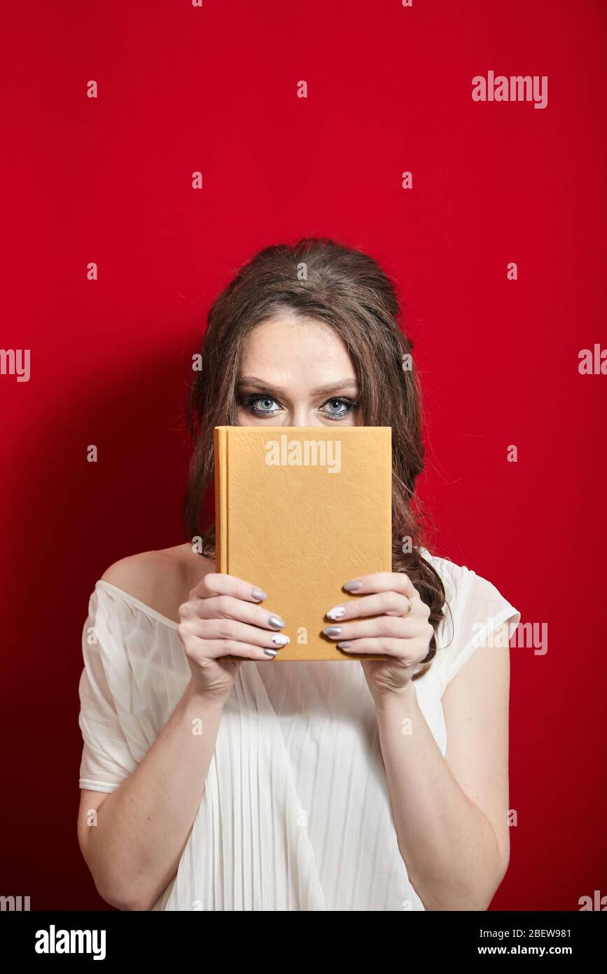 La jeune femme possède un livre blanc en cuir sur le fond de rideaux rouges Banque D'Images