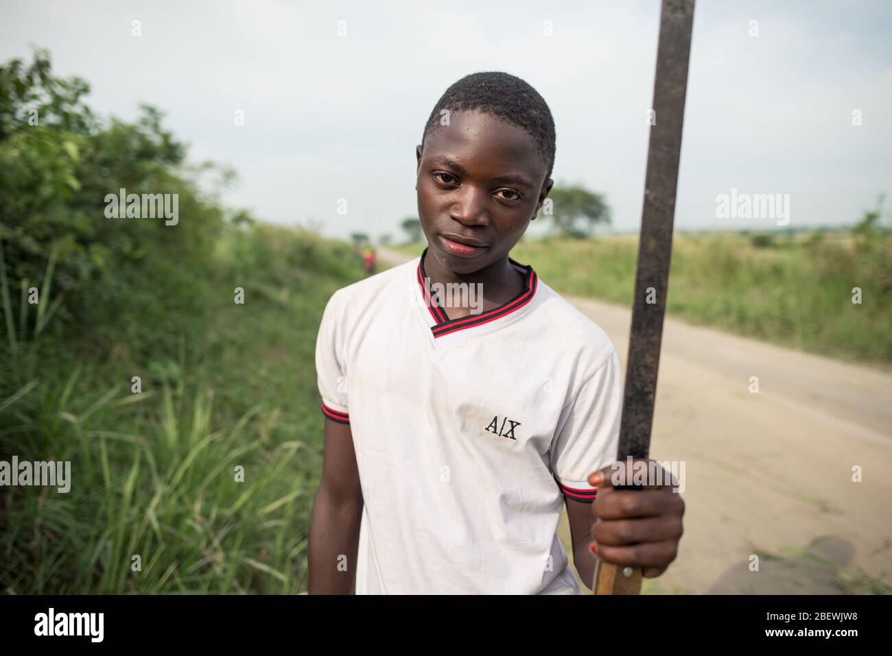 Katwe / Ouganda - 25 octobre 2016 : jeune homme noir africain qui coupe de l'herbe avec une machette, travaillant sur le bord de la route du parc national Reine Elisabeth Banque D'Images