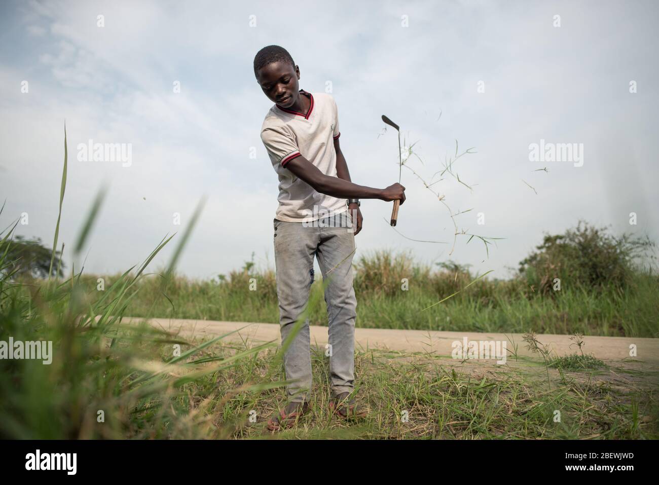 Katwe / Ouganda - 25 octobre 2016 : jeune homme noir africain qui coupe de l'herbe avec une machette, travaillant sur le bord de la route du parc national Reine Elisabeth Banque D'Images