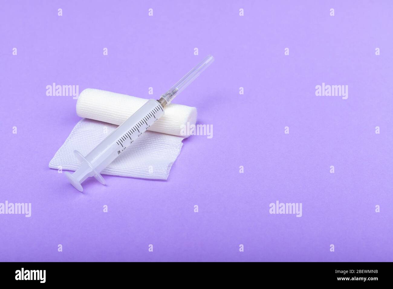 Bandage médical et seringue sur fond lilas. Un rouleau de gaze sur lequel repose la seringue. Pansement à usage médical. Espace pour le texte à droite Banque D'Images