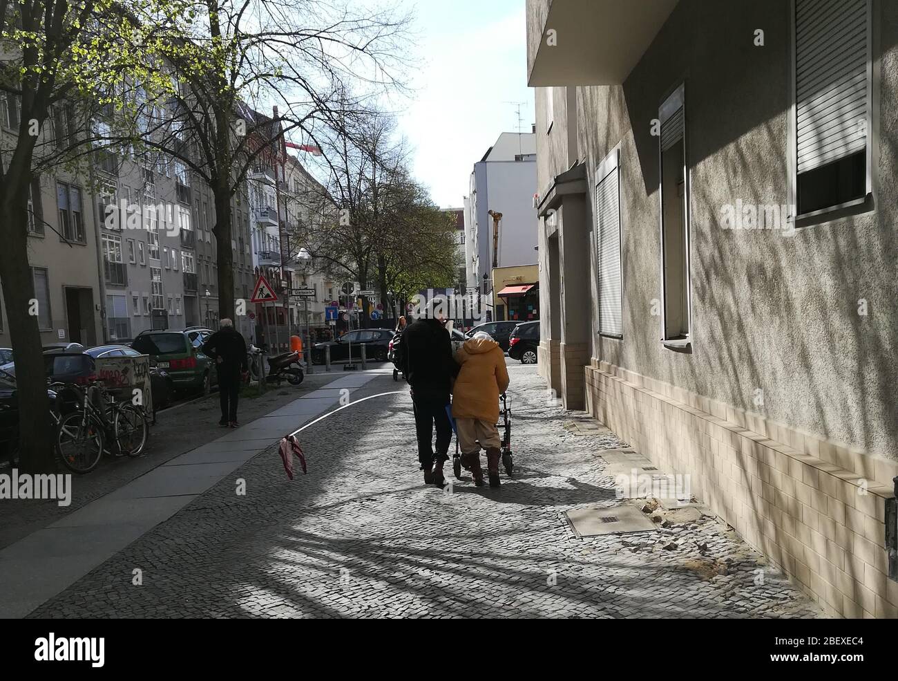 Berlin, Allemagne. 15 avril 2020. Un homme accompagne une femme âgée qui, avec l'aide d'un roller, se promenait dans Spielhagenstraße à Berlin-Charlottenburg. Une barre avec un chiffon est fixée sur le côté du roller de sorte que les autres passants ne puissent pas se rapprocher trop du couple. Crédit: Jan-Uwe Ronneburger/dpa/Alay Live News Banque D'Images