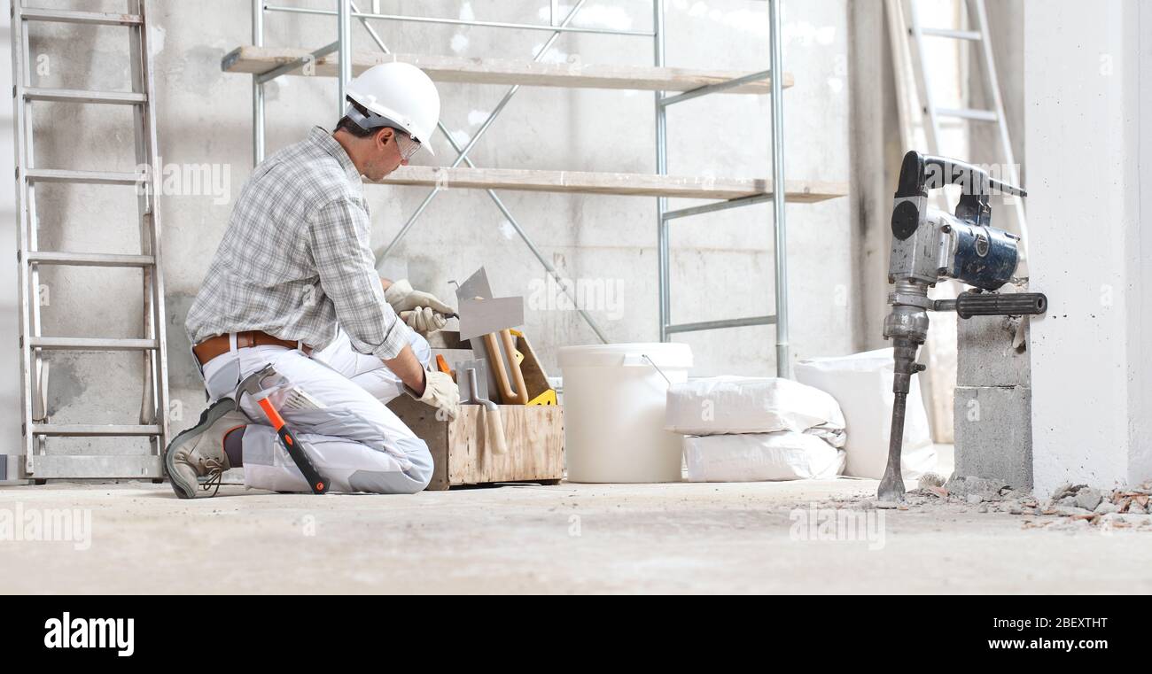 le travailleur de la construction de plâtre travaille avec une boîte à outils  porter des gants, un casque et des lunettes de protection sur le site du  bâtiment intérieur avec échafaudage. seau