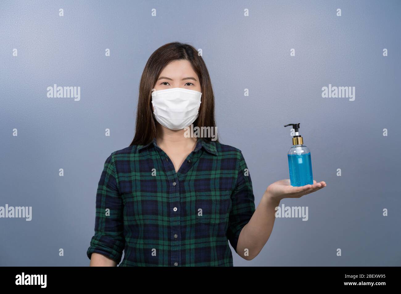 Portrait de la femme asiatique portant un masque chirurgical de visage et présentant du gel d'alcool ou de l'assainisseur de main sur fond bleu, éclosion de covid19 et pandem Banque D'Images
