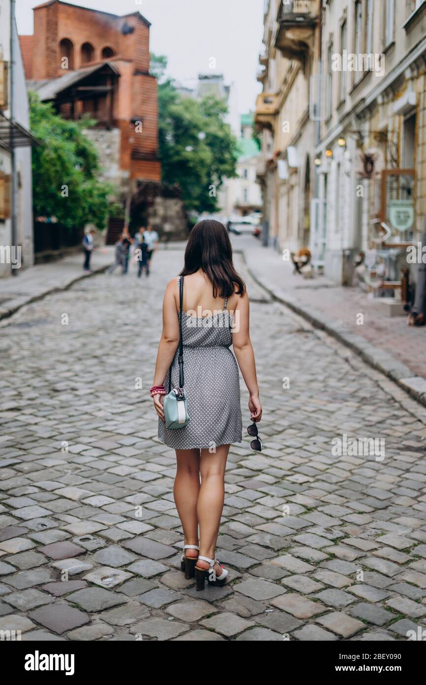 Jeune femme dans une robe grise lors d'une visite de la ville. Femme brunette en robe et sandales marchant dans les rues de la ville. Fille dans un sac à main et des verres Banque D'Images