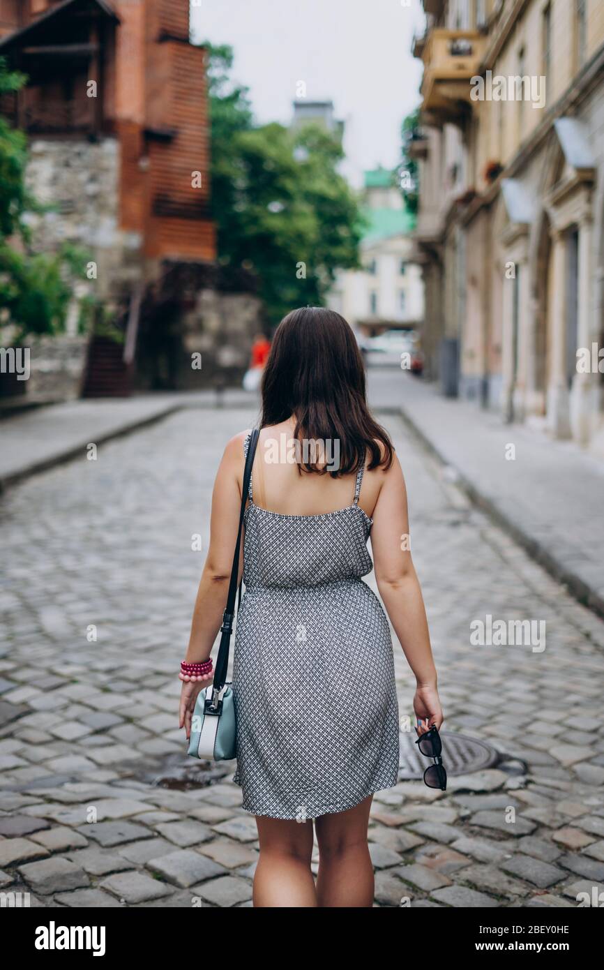 Une jeune femme en visite regarde de belles maisons dans le centre-ville. Fille dans la sundress avec sac à main bleu et lunettes de soleil. Une fille marche la ville dans une robe. Banque D'Images