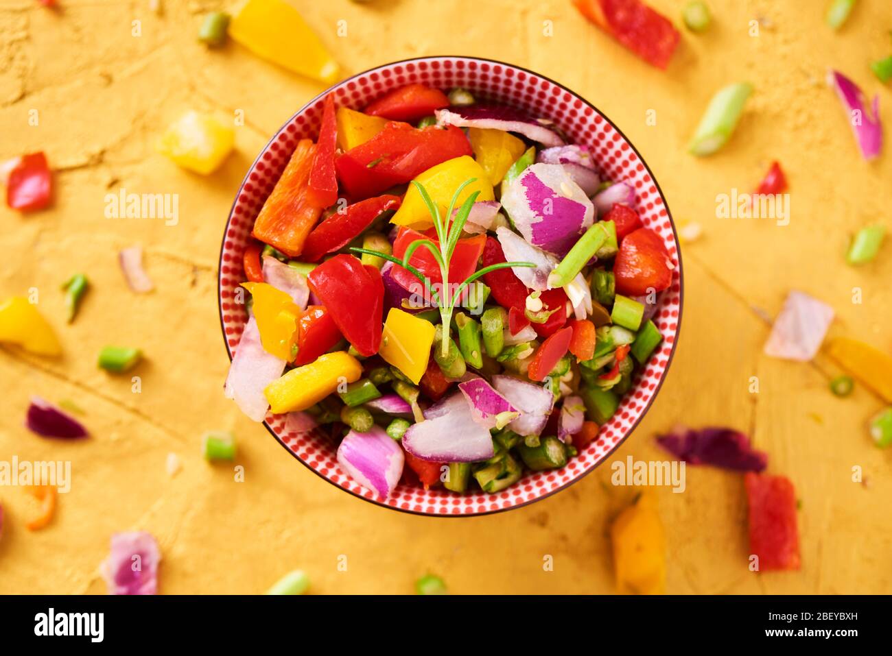 vue en grand angle d'un bol avec un mélange de différents légumes crus hachés, tels que l'asperge, l'oignon ou le poivron jaune et rouge, sur une texture dorée Banque D'Images