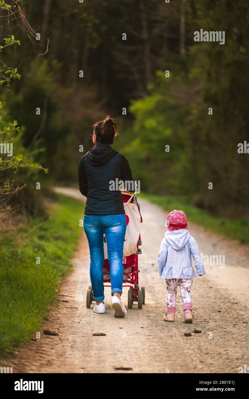 La jeune mère et l'enfant à côté de promenades en poussettes rouges sur le chemin forestier dans la zone rurale Banque D'Images