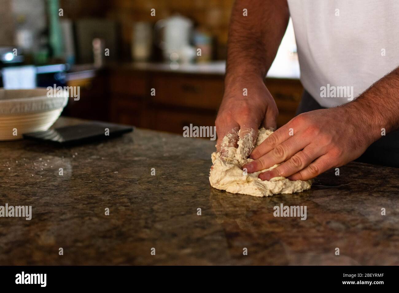 Un homme pétriant de la pâte à pain dans sa cuisine sur une île de cuisine en marbre/granit Banque D'Images