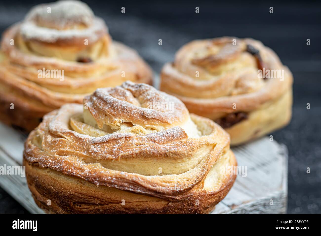 Les produits de boulangerie avec raisins secs et fruits secs sont situés sur un fond en bois sombre. Saupoudrés de sucre glace. Kraffins. Cuisine de Pâques. Espace de copie Banque D'Images