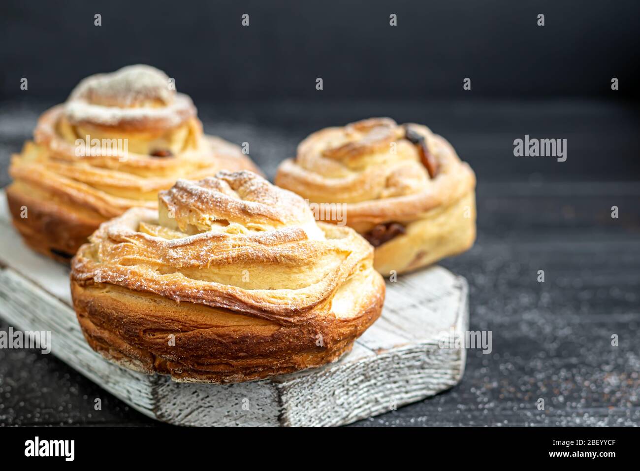 Les produits de boulangerie avec raisins secs et fruits secs sont situés sur un fond en bois sombre. Saupoudrés de sucre glace. Kraffins. Cuisine de Pâques. Espace de copie Banque D'Images