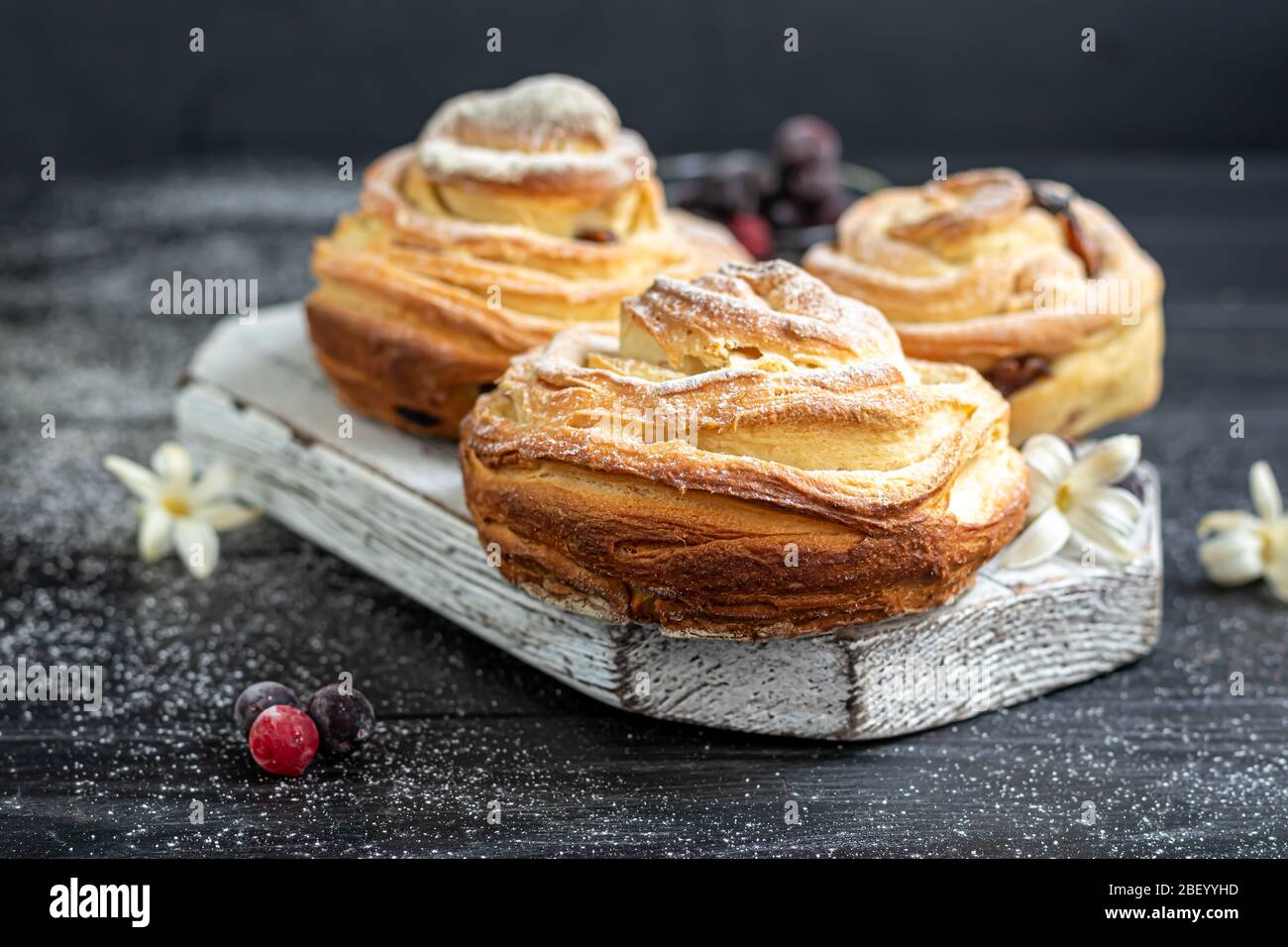 Les produits de boulangerie avec raisins secs et fruits secs sont situés sur un fond en bois sombre. Saupoudrés de sucre glace. Kraffins. Cuisine de Pâques. Espace de copie Banque D'Images