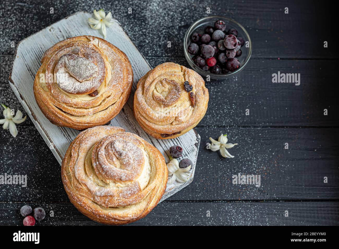 Les produits de boulangerie avec raisins secs et fruits secs sont situés sur un fond en bois sombre. Saupoudrés de sucre glace. Kraffins. Cuisine de Pâques. Espace de copie Banque D'Images