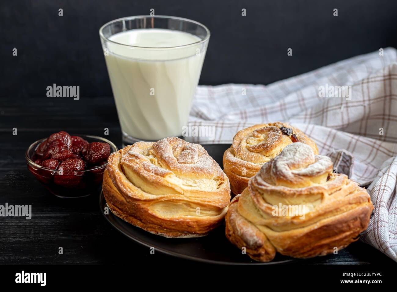 Les produits de boulangerie avec raisins secs et fruits secs sont situés sur un fond en bois sombre. Saupoudrés de sucre glace. Kraffins. Cuisine de Pâques. Espace de copie Banque D'Images