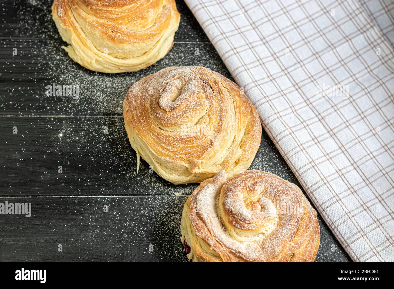 Les produits de boulangerie avec raisins secs et fruits secs sont situés sur un fond en bois sombre. Saupoudrés de sucre glace. Kraffins. Cuisine de Pâques. Espace de copie Banque D'Images