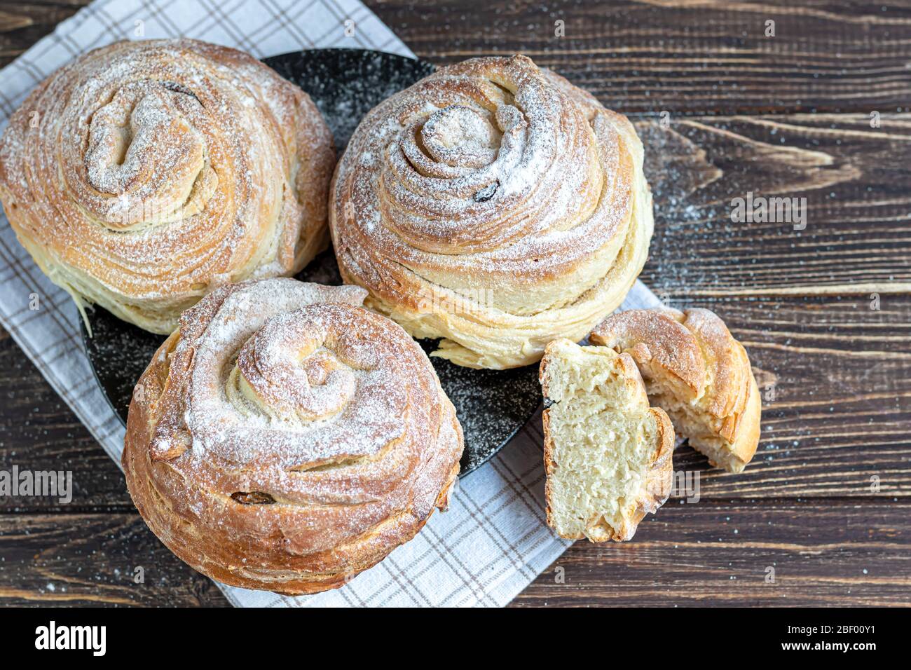 Les produits de boulangerie avec raisins secs et fruits secs sont situés sur un fond en bois sombre. Saupoudrés de sucre glace. Kraffins. Cuisine de Pâques. Espace de copie Banque D'Images