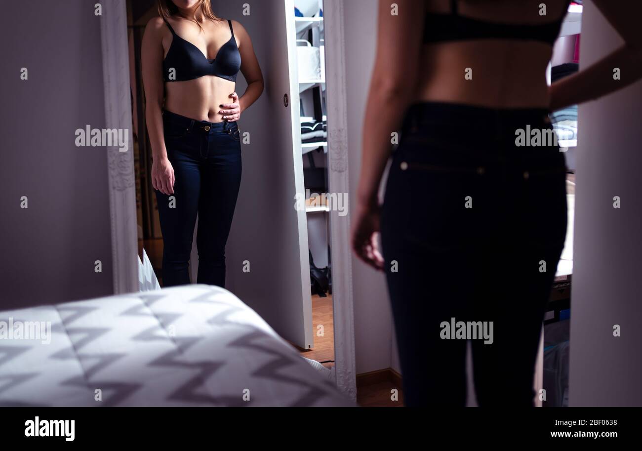 Femme mince regardant dans le miroir. Perte de poids et régime. Tenant la main sur son estomac. Stress et souci de gagner de la graisse. Troubles de l'alimentation. Banque D'Images