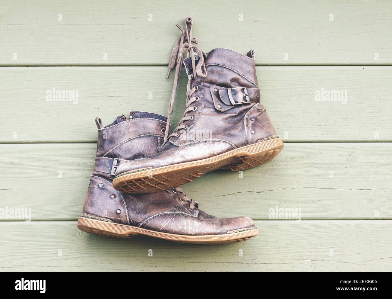 Paire de chaussures en cuir anciennes portées accrochées sur un mur en bois, bottes abandonnées Banque D'Images