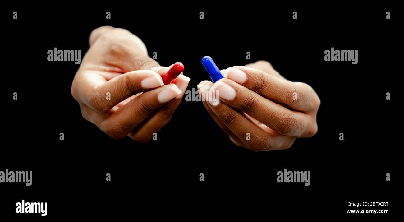 Mains d'une femme noire offrant les pilules rouge et bleue sur un fond noir. Concept de vérité laid vs beau mensonge, réalité vs fiction. SELECTIV Banque D'Images