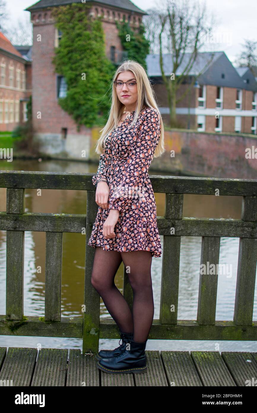 jeune, jolie femme portant des lunettes avec des cheveux coulant, longs, avec une expression faciale sérieuse dans une robe de fleur sur un pont en bois Banque D'Images jeune, jolie femme portant des lunettes avec des cheveux coulant, longs, avec une expression faciale sérieuse dans une robe de fleur sur un pont en bois Banque D'Images