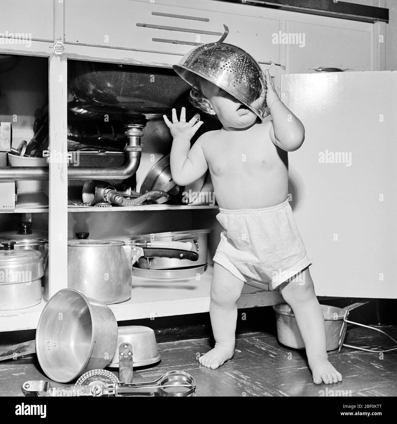 Annees 1950 Bebe Fille Tres Petit Jouant Sous Evier De Cuisine Trouver Des Casseroles Pots Ustensiles Et Porter La Passoire Sur La Tete Cam001 Hars Colander Bonheur Decouverte Etrange Grotesque